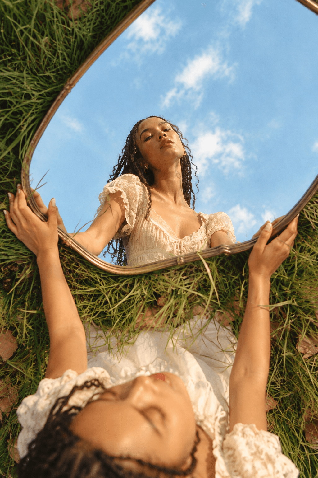 A woman in a white dress lies on grass in late sun, one arm raised, pink satin ribbon wound across her.