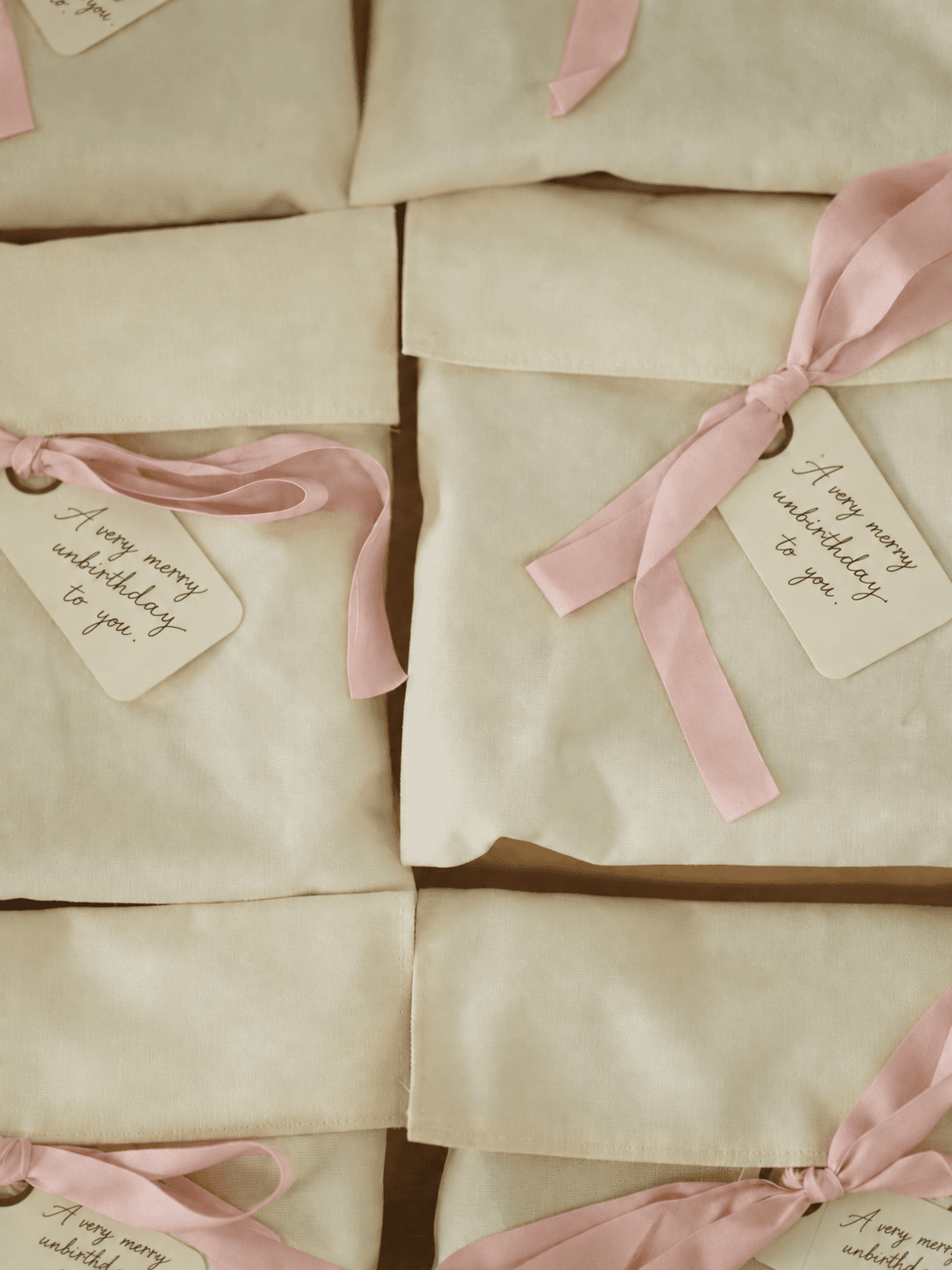 Cream cotton pouches tied with pink ribbon, each tag reading a very merry unbirthday to you.